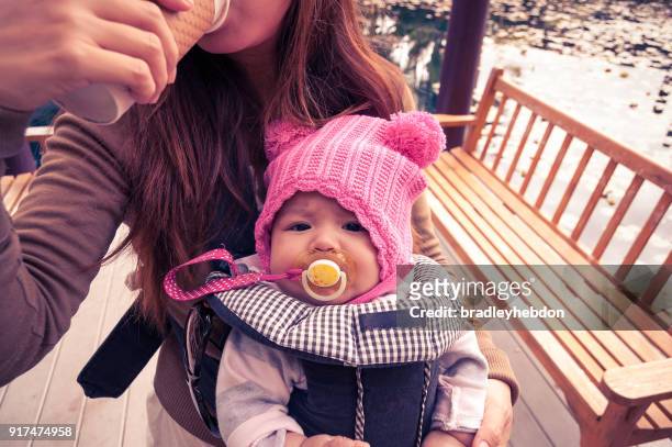 Mor håller hennes lilla flicka i bärsele när man dricker kaffe