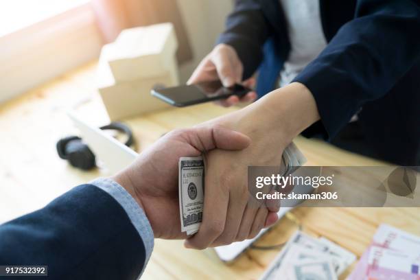 business man shake hand after agree deal with us dollar money in his hand over workspace - corrupción fotografías e imágenes de stock