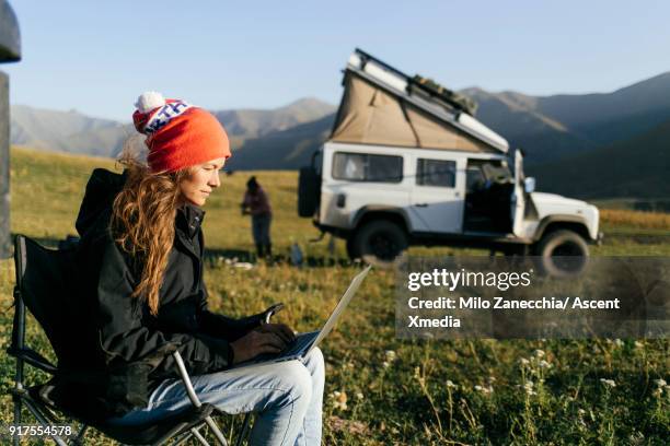 woman working on computer while 4x4 camping in mountain meadow - movil stock-fotos und bilder