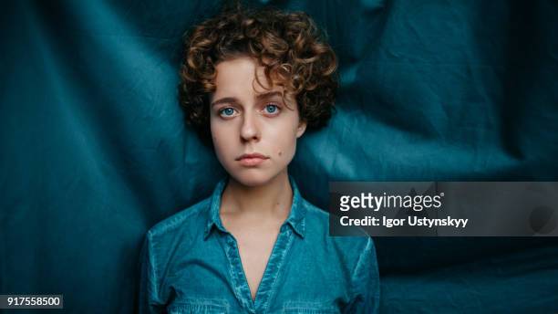 attractive female with curly hair on blue background - studio shot lonely woman stock pictures, royalty-free photos & images
