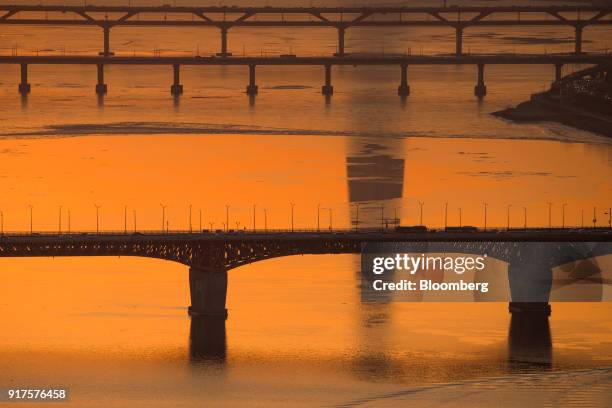 The Lotte World Tower, which houses the Lotte Group headquarters, is reflected in a river as vehicles drive over a bridge at sunrise in Seoul, South...