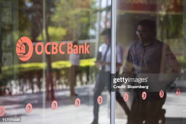 Pedestrians walk past an Oversea-Chinese Banking Corp. Logo displayed on a glass panel in the central business district of Singapore, on Monday, Feb....