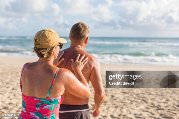 mature aged couple putting on sunscreen at the beach - putting lotion stock pictures, royalty-free photos & images