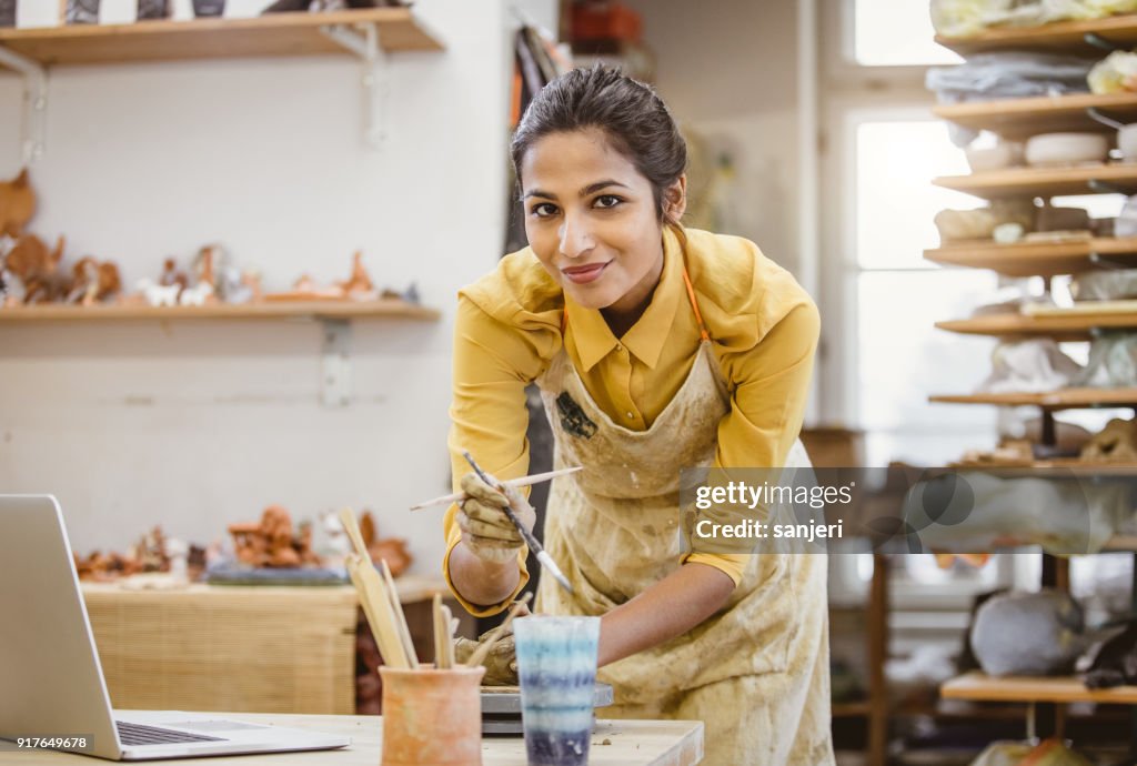 Portrait of a Young Woman Creating Pottery, Using Laptop