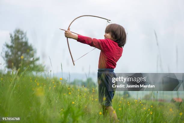 little child with bow and arrow in field - longbow stock pictures, royalty-free photos & images