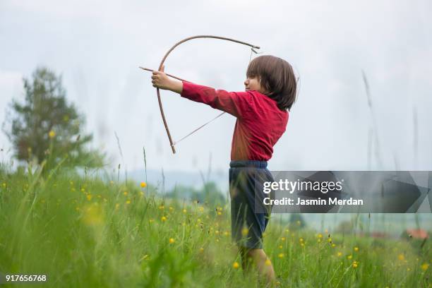 little child with bow and arrow in field - arco de arqueiro imagens e fotografias de stock