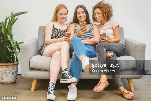 young women laughing checking social media messages - multiple devices at home stock pictures, royalty-free photos & images