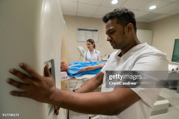 doctora, explicando el procedimiento de una resonancia magnética a la paciente vestida con una bata de hospital y técnico prepara la máquina - mri technician fotografías e imágenes de stock