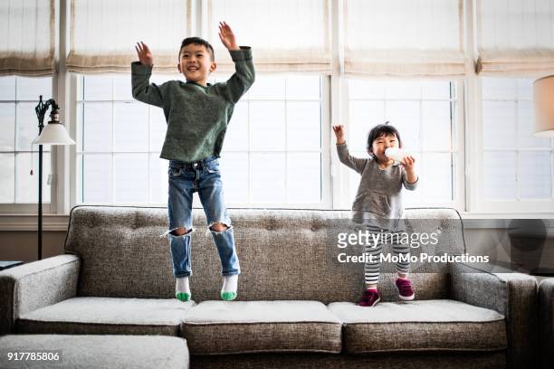 kids jumping on couch at home - sibling stock pictures, royalty-free photos & images