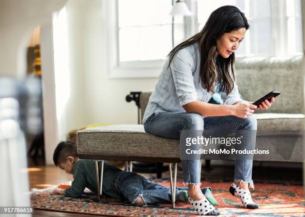 woman using smartphone at home with child in background - stay at home mother stock pictures, royalty-free photos & images