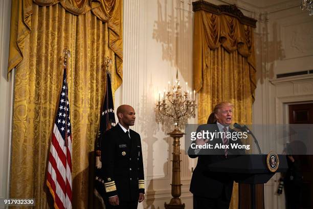 President Donald Trump speaks as Surgeon General Jerome Adams looks on during a reception in the East Room of the White House February 13, 2018 in...