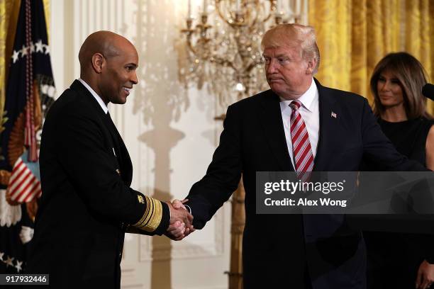 President Donald Trump shakes hands with Surgeon General Jerome Adams as first lady Melania Trump looks on during a reception in the East Room of the...