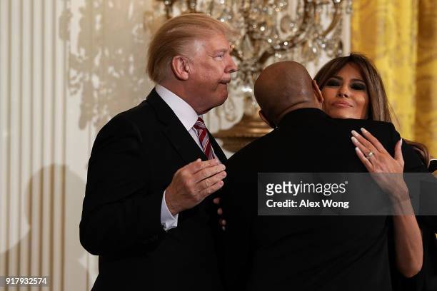 Surgeon General Jerome Adams hugs first lady Melania Trump as President Donald Trump looks on during a reception in the East Room of the White House...
