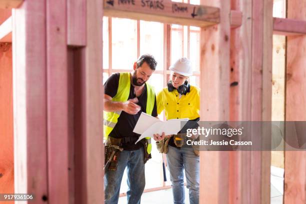 male and female construction workers discuss the building plans inside the building site - contratista de obras fotografías e imágenes de stock