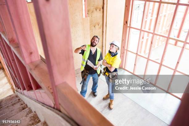 male and female construction workers discuss the building plans inside the building site - bauingenieurwesen stock-fotos und bilder