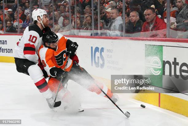 Jimmy Hayes of the New Jersey Devils prepares to drive Radko Gudas of the Philadelphia Flyers into the boards as they battle for the loose puck on...