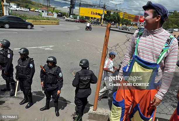 Clown looks at policemen standing guard at the Kenedy neighborhood during a protest of supporters of deposed Honduran president Manuel Zelaya in...