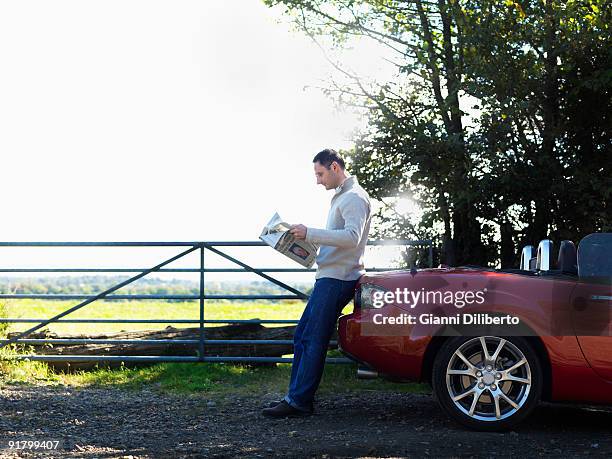 man reading newspaper by car on country road - man in car reading newspaper stock pictures, royalty-free photos & images