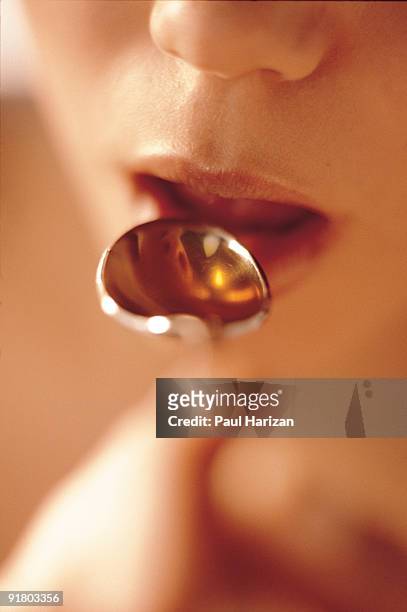 woman spooning medicine into mouth - human mouth stockfoto's en -beelden