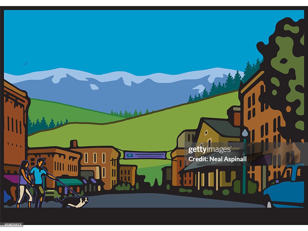 A couple walking a dog in a town with mountains in the background
