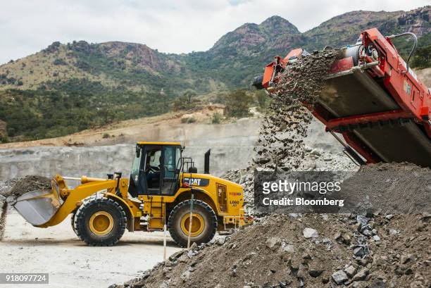 Conveyor deposits raw aluminum ore onto a stockpile as a Caterpillar Inc. Excavator passes at the Northam Platinum Ltd. Booysendal platinum mine...
