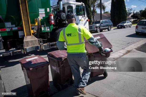 Waste Management Inc. Employee collects trash bins outside a home in Hayward, California, U.S., on Monday, Feb. 12, 2018. Waste Management Inc. Is...