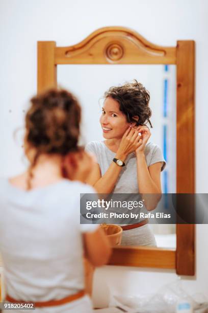 pretty woman putting on earrings in front of the mirror - rhinestone 個照片及圖片檔