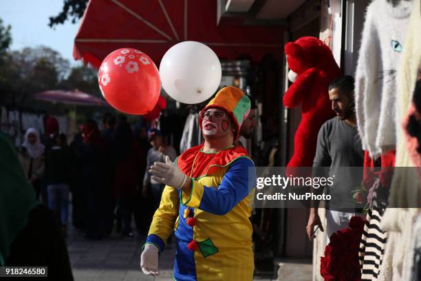 Palestinian clown presents roses and balloons to people in front of a shop on Valentine's day in Gaza city on February 14, 2018. Valentine's Day is...