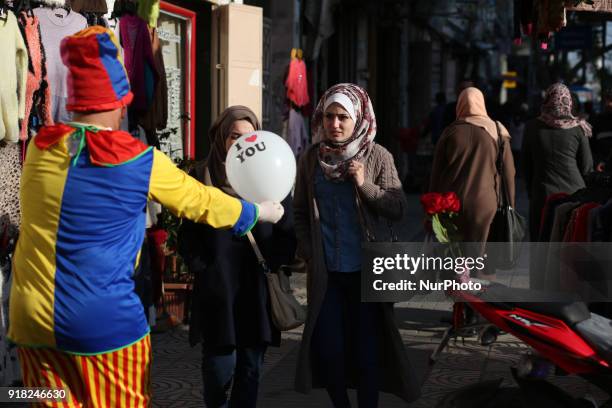 Palestinian clown presents roses and balloons to people in front of a shop on Valentine's day in Gaza city on February 14, 2018. Valentine's Day is...