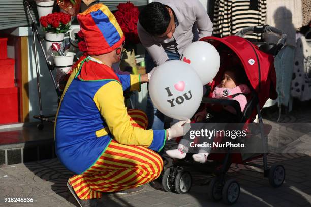 Palestinian clown presents roses and balloons to people in front of a shop on Valentine's day in Gaza city on February 14, 2018. Valentine's Day is...