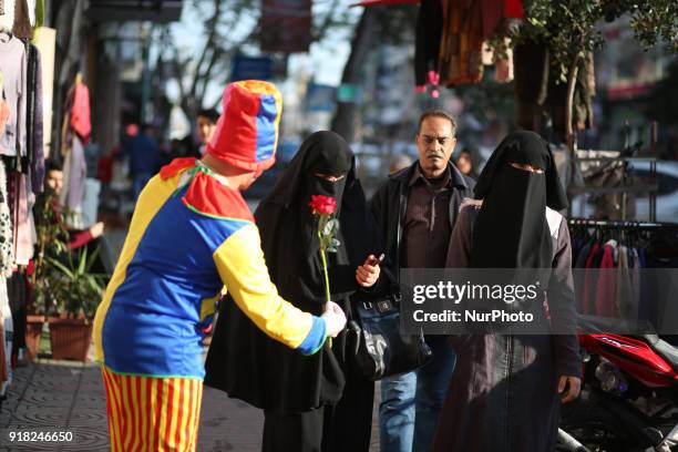 Palestinian clown presents roses and balloons to people in front of a shop on Valentine's day in Gaza city on February 14, 2018. Valentine's Day is...