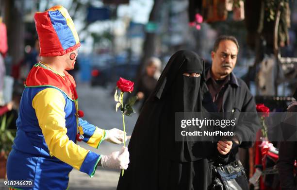 Palestinian clown presents roses and balloons to people in front of a shop on Valentine's day in Gaza city on February 14, 2018. Valentine's Day is...