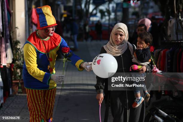 Palestinian clown presents roses and balloons to people in front of a shop on Valentine's day in Gaza city on February 14, 2018. Valentine's Day is...