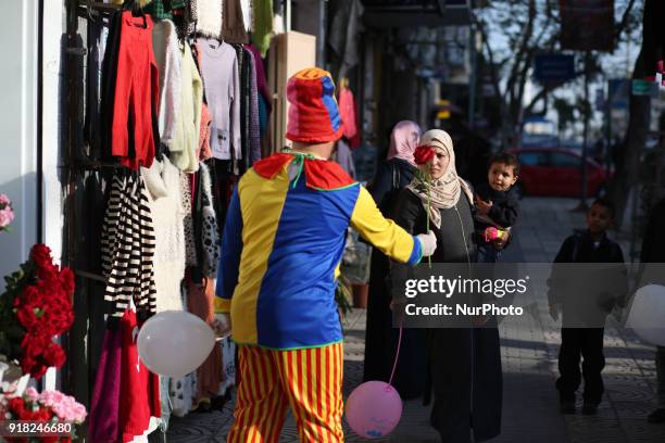 Palestinian clown presents roses and balloons to people in front of a shop on Valentine's day in Gaza city on February 14, 2018. Valentine's Day is...