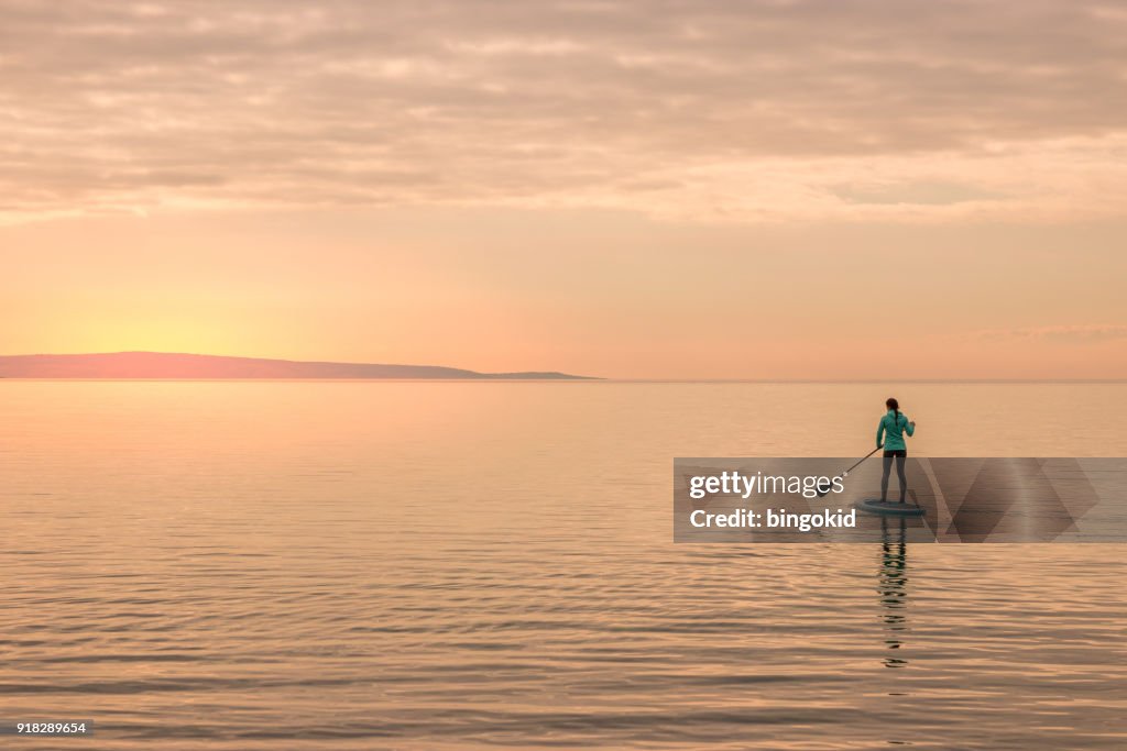 Fille de pagayer vers le coucher du soleil