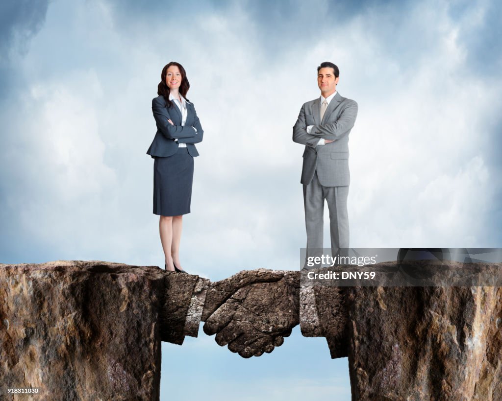 Businesswoman And Businessman Stand On Cliffs Joined By Stone Handshake