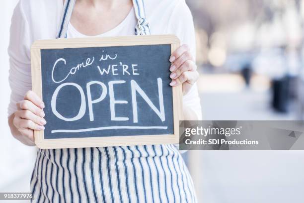 cafe owner holding 'open' sign outdoors - open sign stock pictures, royalty-free photos & images