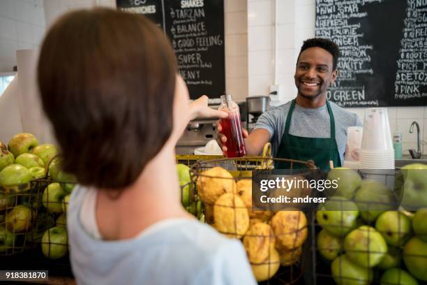 friendly business owner working at his juice bar handing a bottled juice to an unrecognizable female customer - juice bar stock pictures, royalty-free photos & images