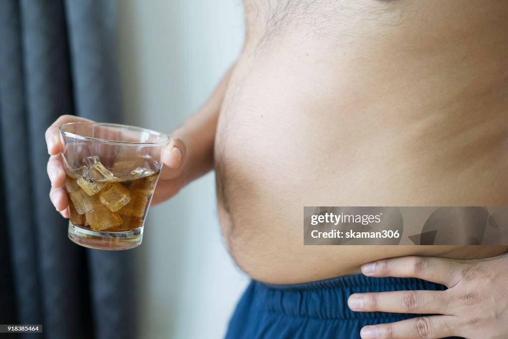 Overweight man holding glass of aerated soft drink