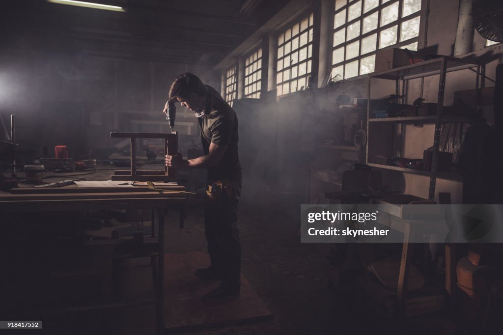 Männliche Zimmermann mit Bohrer, einen Stuhl in einer Werkstatt reparieren.