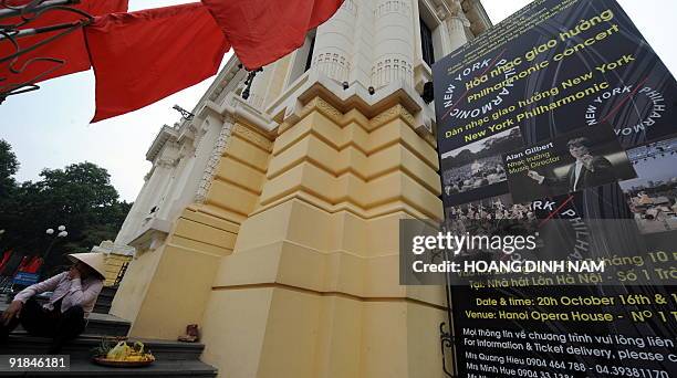 Street vendor sits next to a poster hung outside the Hanoi Opera house advertising a performance of the New York Philharmonic in Hanoi on October 13,...