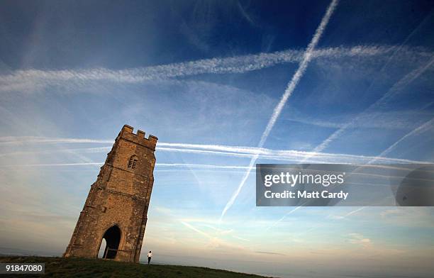 Woman looks up to the mass of contrails left by jet aircraft crossing the sky above the distinctive landmark of the historic 15th century St....