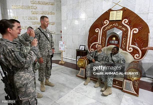 Soldiers take souvenir photos with a chair that belonged to executed Iraqi dictator Saddam Hussein at the former presidential palace, which became a...