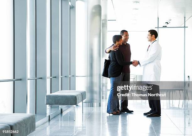doctor shaking hands with couple in lobby - three female doctors stock pictures, royalty-free photos & images