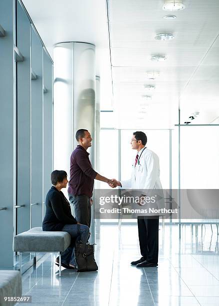 doctor shaking hands with couple in lobby - couple shaking hands with doctor stock pictures, royalty-free photos & images