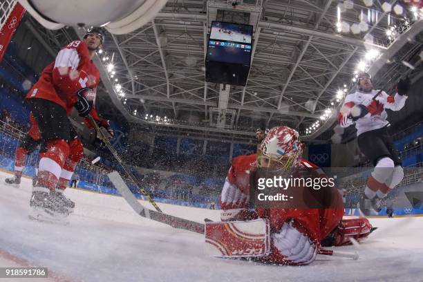 Canada's Wojciech Wolski jumps over Switzerland's Jonas Hiller as Switzerland's Cody Almond watches in the men's preliminary round ice hockey match...