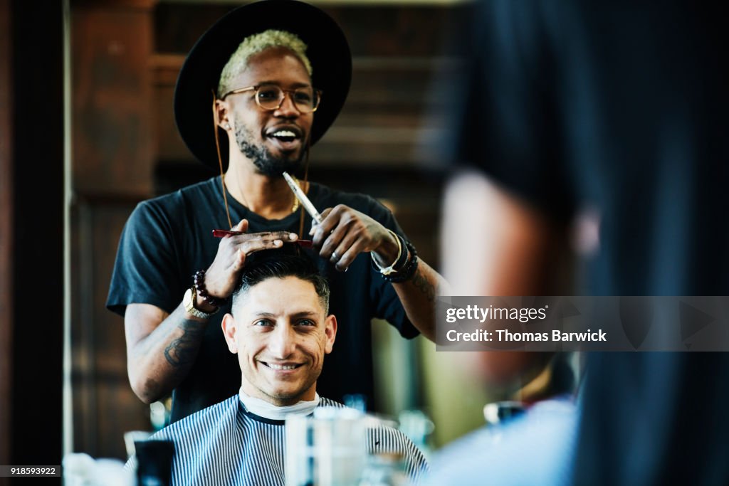Smiling barber in discussion with client while cutting hair in barber shop
