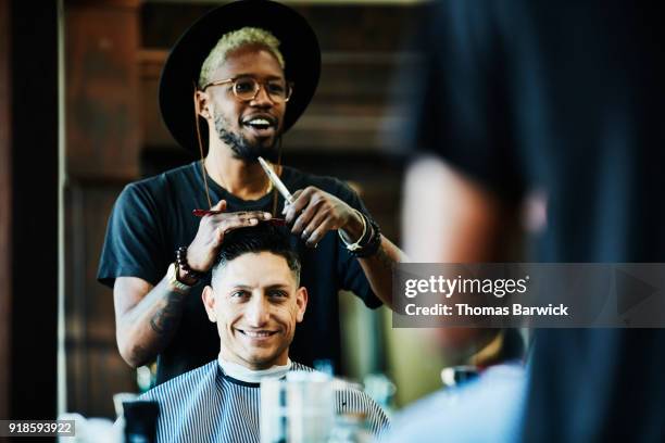 smiling barber in discussion with client while cutting hair in barber shop - barbers stockfoto's en -beelden