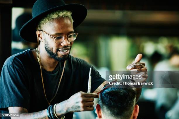 smiling barber cutting clients hair in barber shop - at hairdresser stock-fotos und bilder