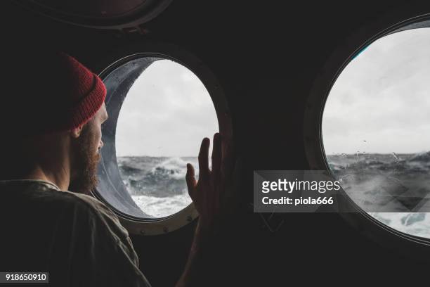uomo alla finestra dell'oblò di una nave in un mare agitato - sailor foto e immagini stock